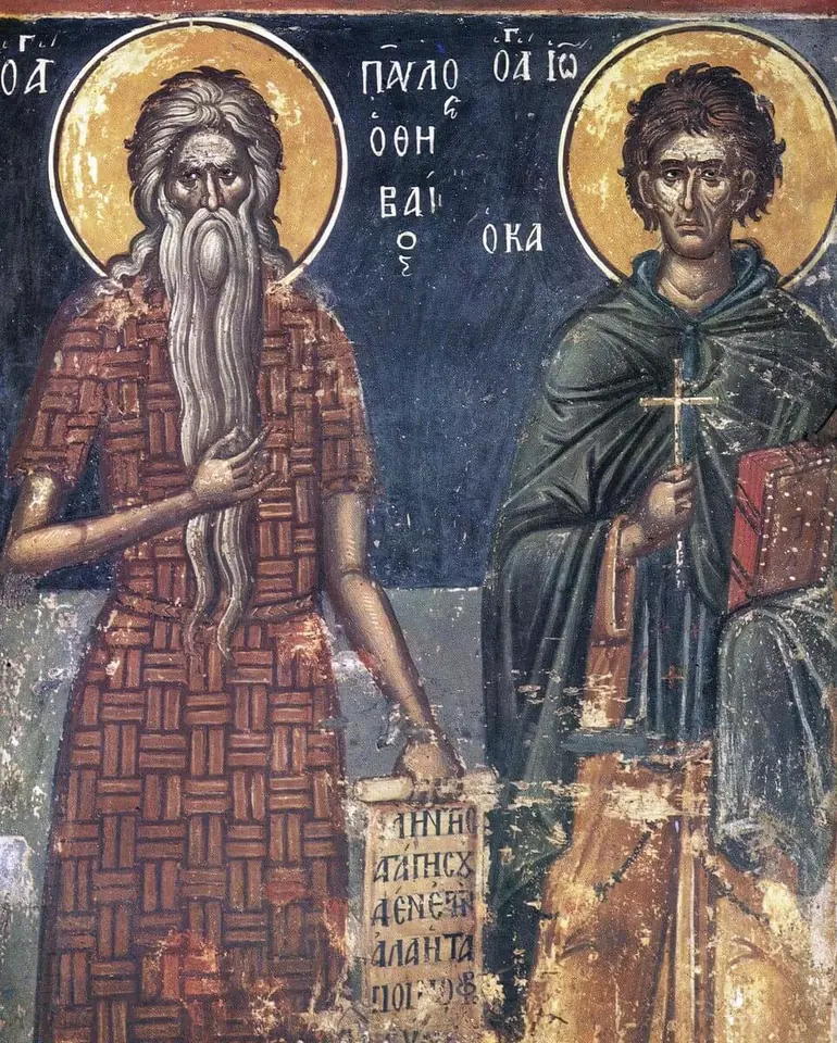 Fresco of an old saint with a very long white beard in a red-brown tunic patterned like woven palm leaves, holding a scroll, beside a young saint in a dark green cloak holding a cross and a book