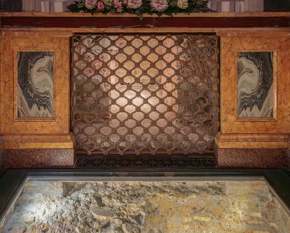 A marble slab of an ancient tomb seen through a window in the floor, below a grille set into colored marble, in the confessio of St. Paul Outside the Walls