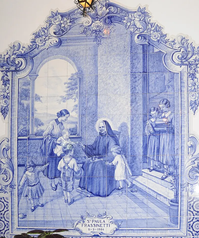 Blue-and-white Portuguese tile panel showing a nun seated on a terrace with children gathered around her, framed in ornate scrollwork