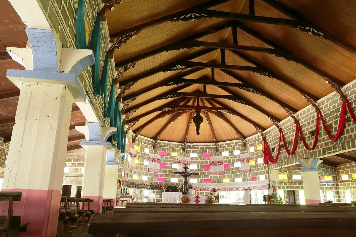 Open church interior with white pillars, a high wooden roof, rows of benches and colored banners around the sanctuary
