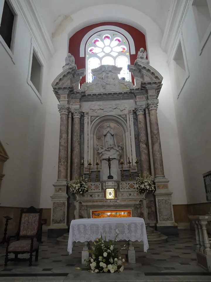 Altar mayor de mármol de la iglesia de San Pedro Claver con una urna de cristal bajo la mesa del altar y un crucifijo y una imagen encima