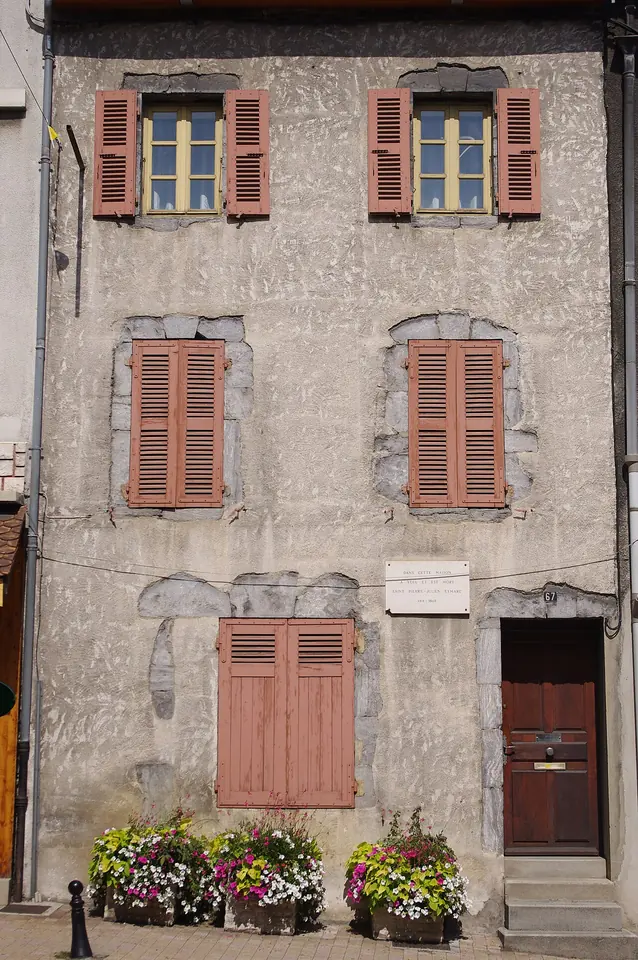 Narrow gray stone house with salmon-colored shutters and flower pots at the door, the birthplace of St. Peter Julian Eymard in La Mure