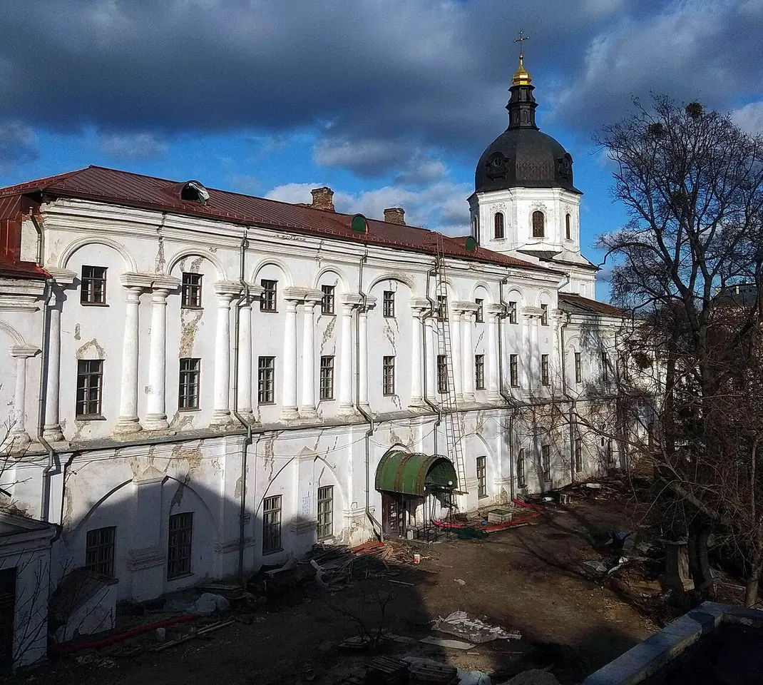 Long white two-story building with a red roof and a small domed bell tower, seen across a courtyard with bare trees