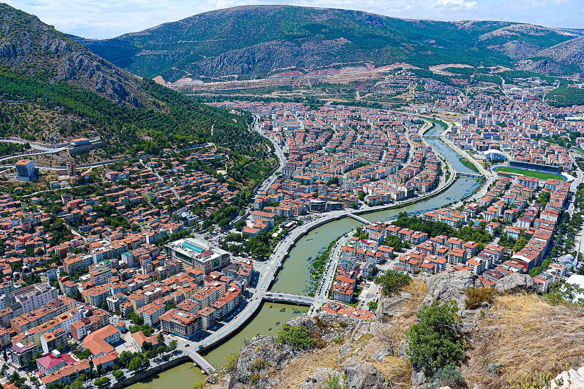 A river winding through a town of red-roofed houses in a valley between steep green mountains