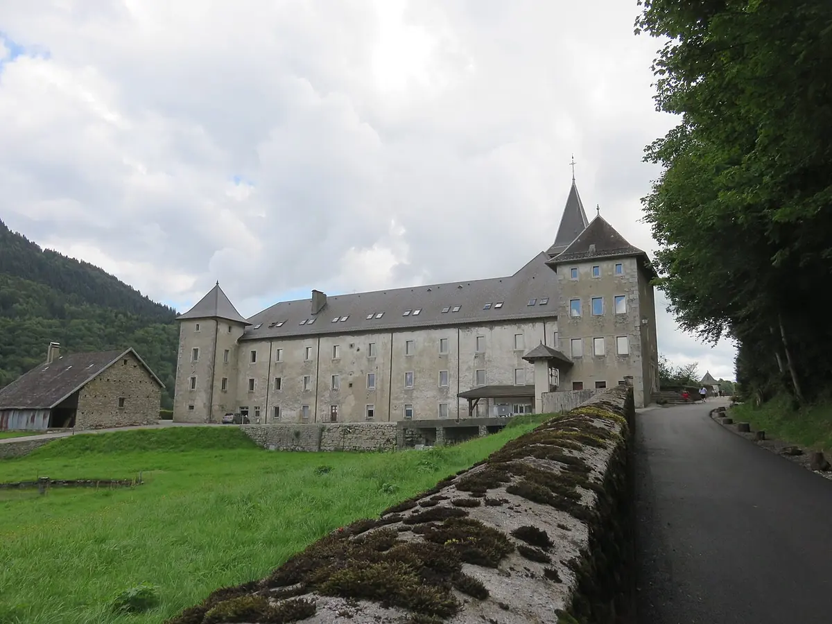 A long gray stone monastery with a steep slate roof and a small tower beside a mountain road and green meadow