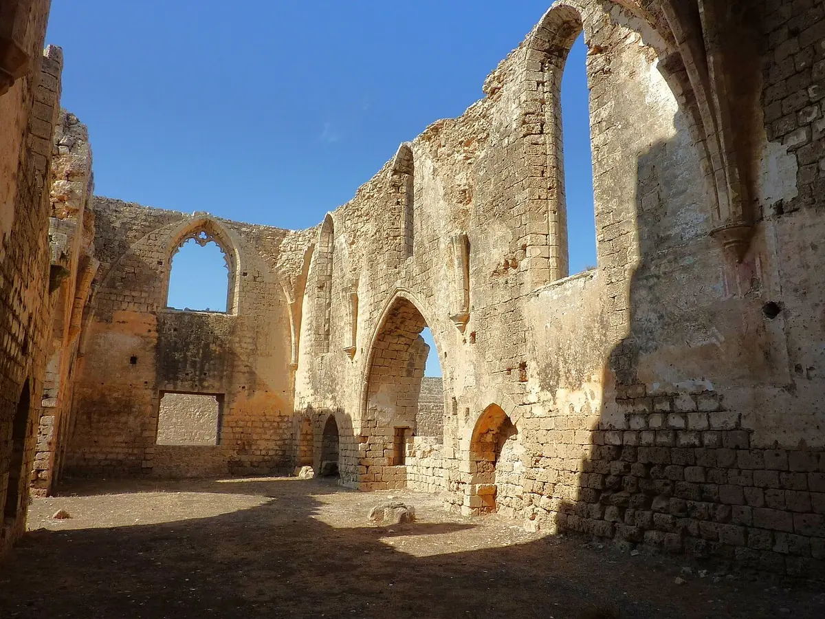Roofless interior of a Gothic church with high pointed windows and arches in golden stone, open to the sky