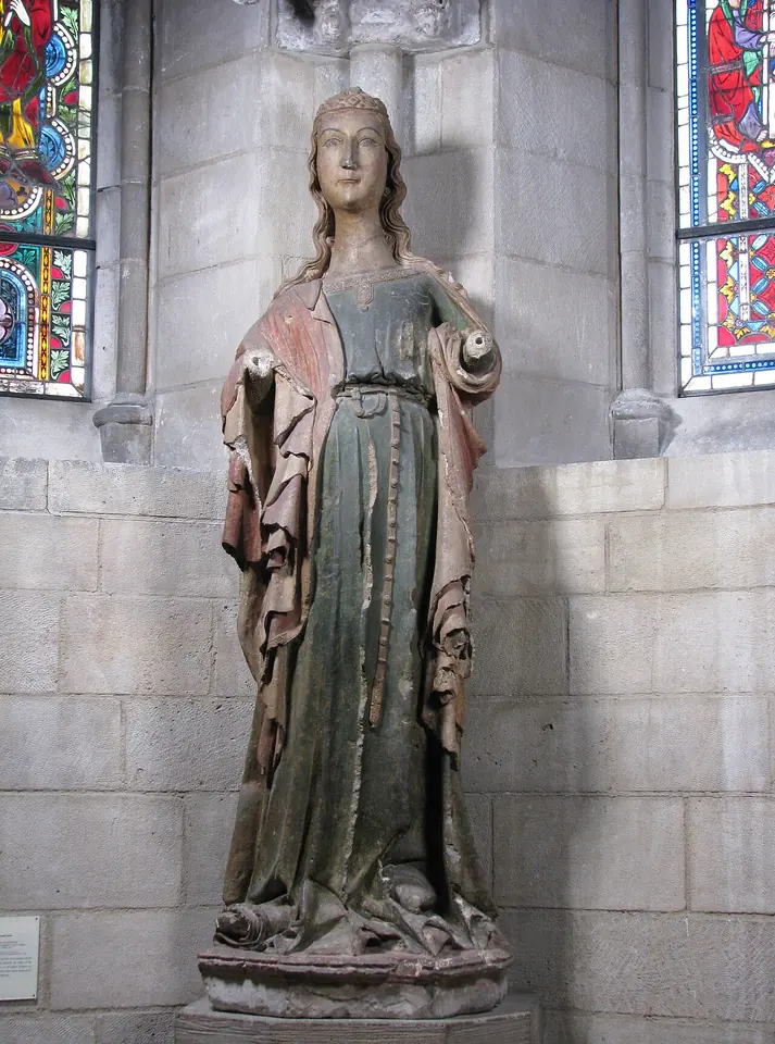 Painted wooden statue of a young woman with long hair and a rose-colored mantle over a green gown, standing in a stone niche
