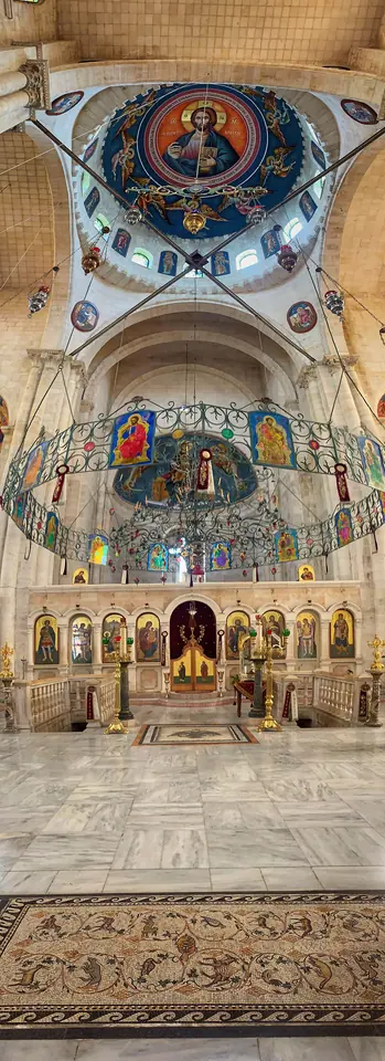 Tall church interior with a painted dome of Christ, a ring-shaped chandelier hung with icons, and a gilded iconostasis