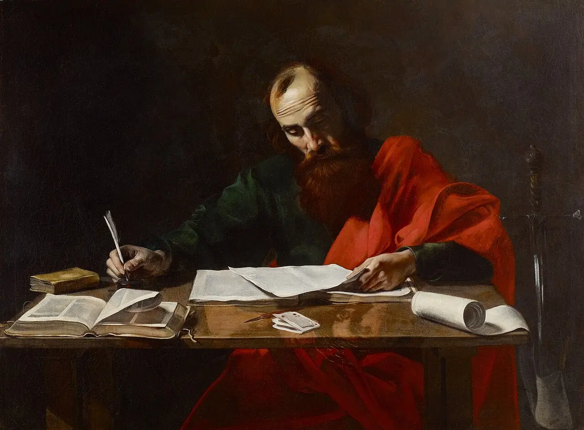Baroque painting of a balding, bearded St. Paul in a red cloak bent over a table, writing with a quill on loose sheets beside open books, with the hilt of a sword at his side