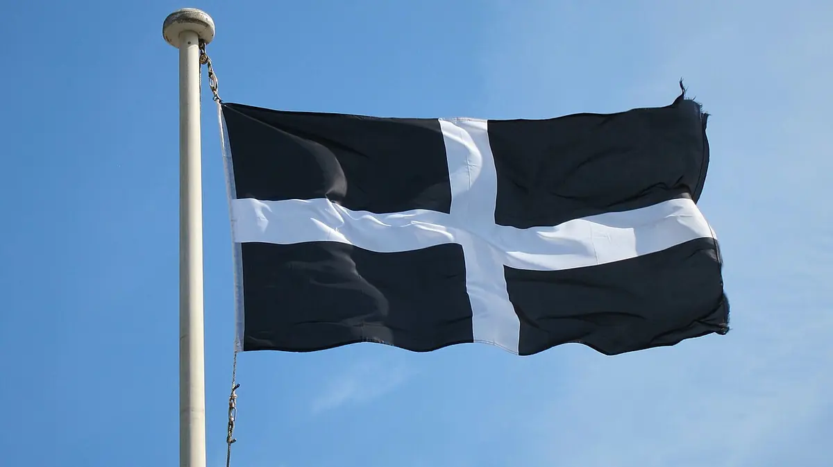 A black flag with a white cross flying from a white pole against a clear blue sky