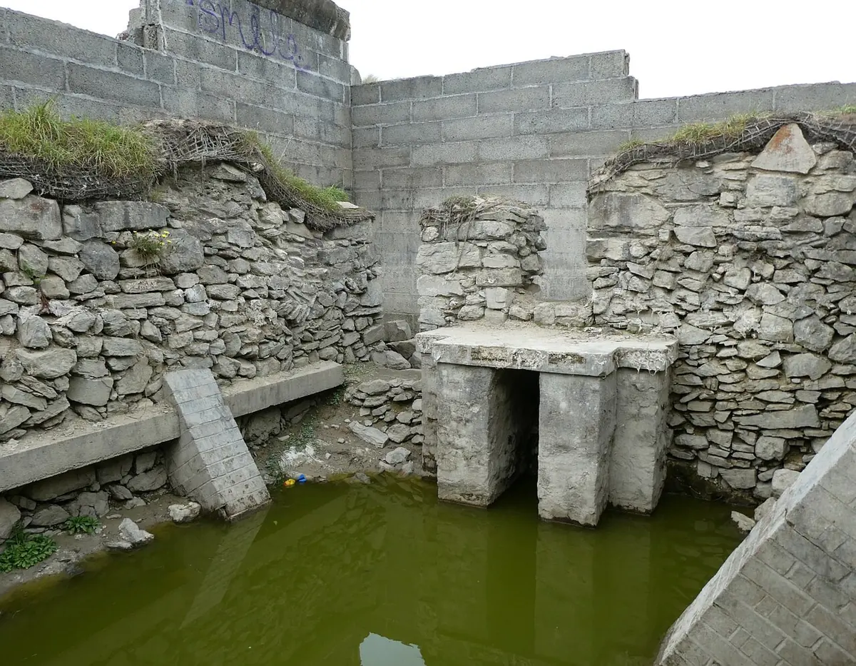 Inside the ruined oratory, a plain stone altar stands against the rough rubble east wall, with a stone bench along the side and water on the floor