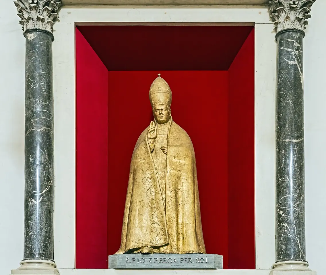 A gilded bronze statue of St. Pius X wearing a tall papal tiara, standing in a red niche between two green marble columns