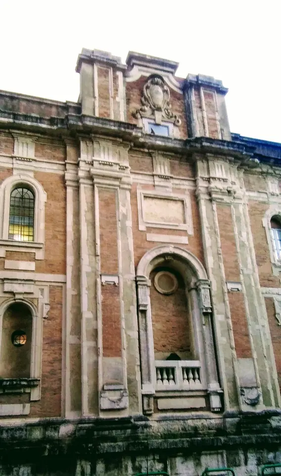 The upper part of a brick and stone Baroque church facade with pilasters and a niche, against a pale sky