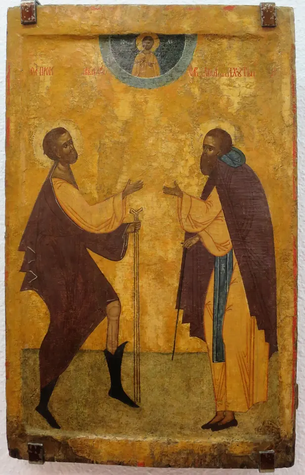 An icon on a yellow ground of two saints facing each other, a barefoot fool in a brown cloak with staffs and a monk with a long beard, below a small image of Christ