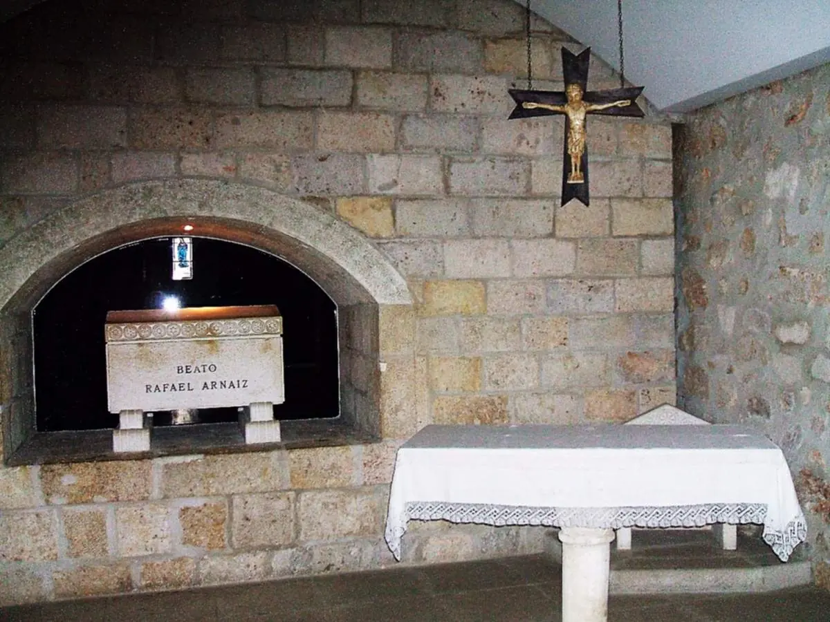 A plain white stone tomb inscribed with his name set in an arched niche of a stone wall, with a small altar and a crucifix