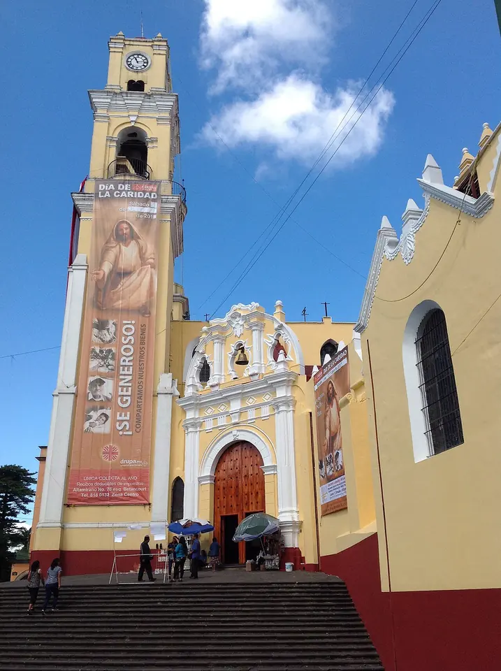 Front of a yellow and white colonial cathedral with a tall bell tower at the top of a flight of steps, under a blue sky with clouds