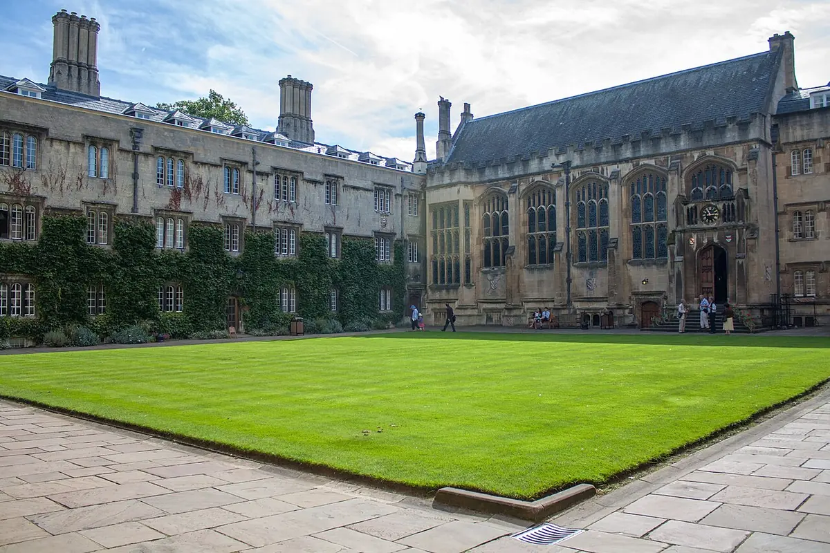 Green lawn of an Oxford college quadrangle surrounded by gray stone buildings with tall chimneys and Gothic windows