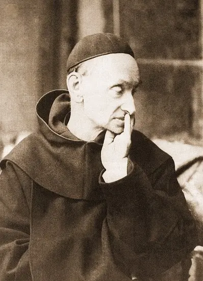 Old sepia photograph of an elderly friar with a skullcap and a brown hooded habit, seated, with his chin resting on his hand and his eyes turned aside in thought