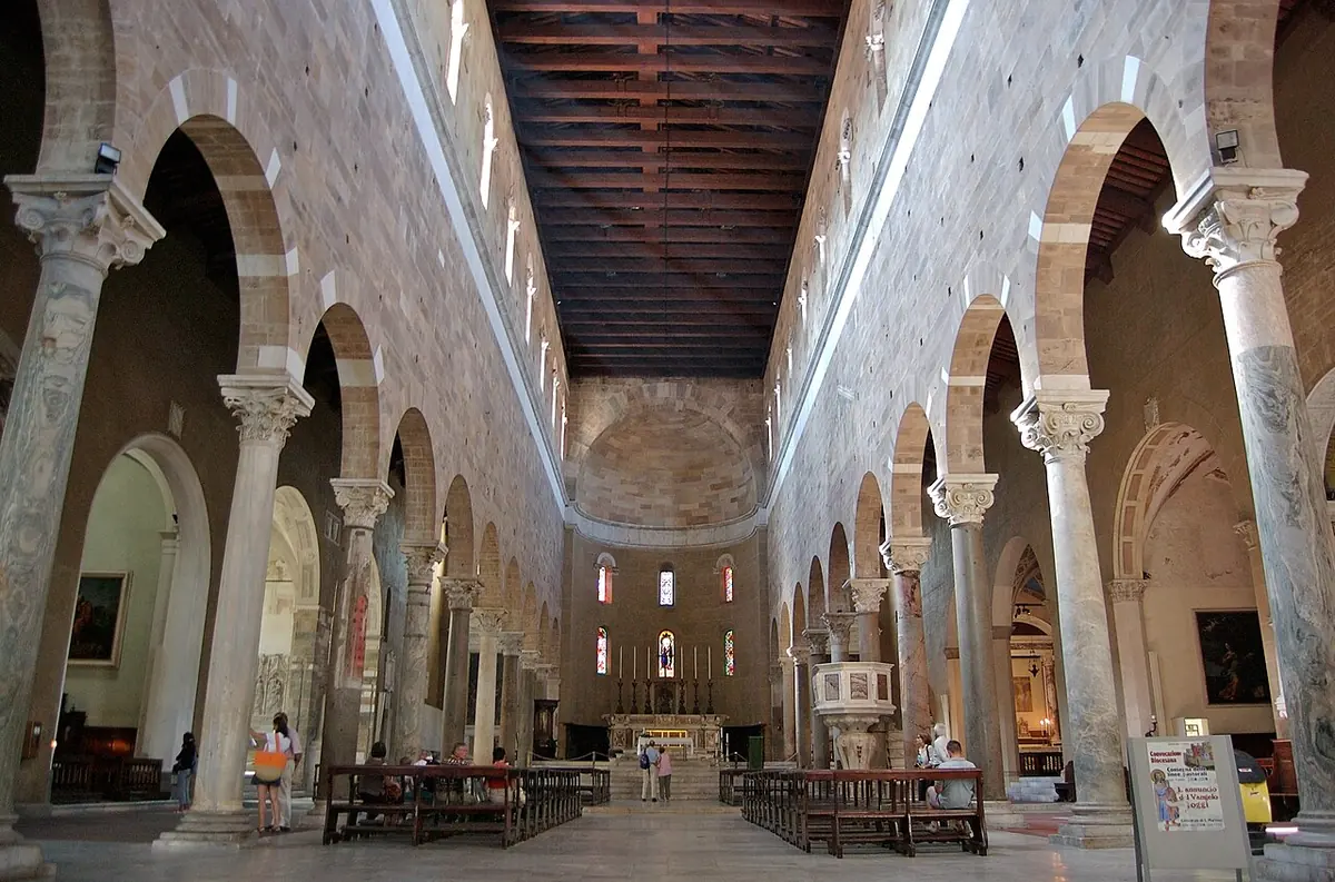 Long Romanesque church nave with rows of columns and round arches, a wooden ceiling and the apse at the far end