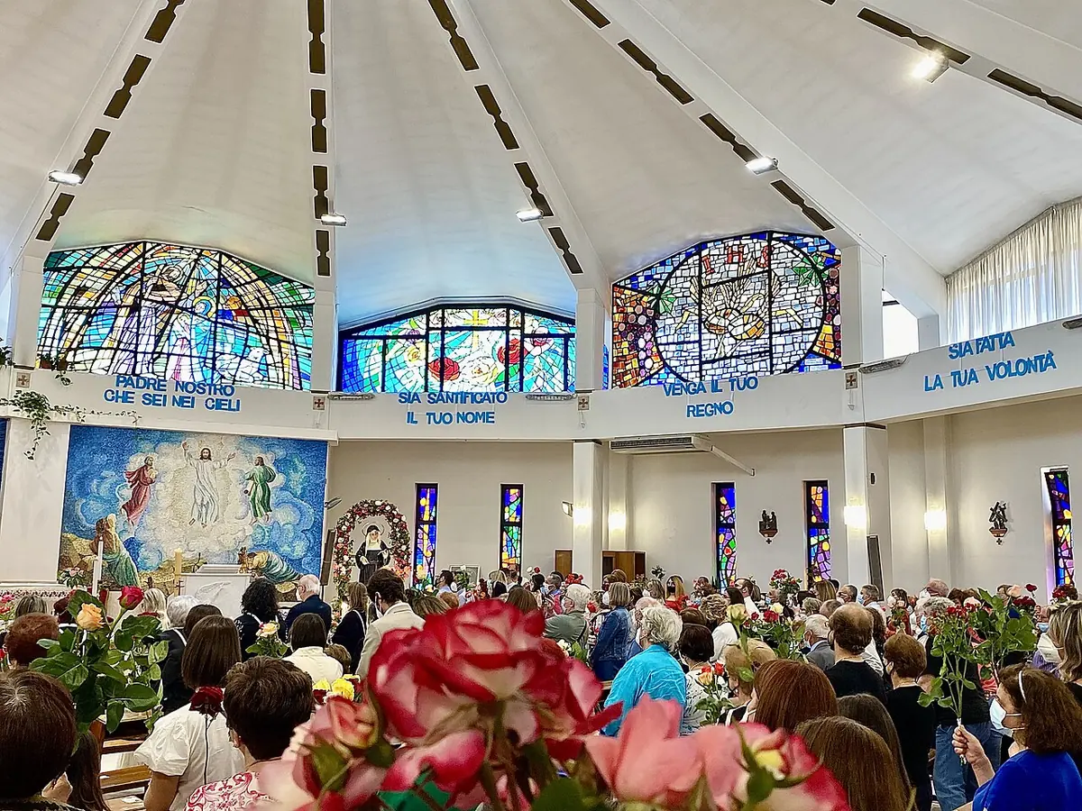 A crowded modern church on St. Rita's feast, with worshippers holding up long-stemmed red and pink roses for the blessing