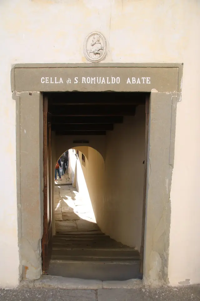 Plain stone doorway with an inscription naming the cell of St. Romuald, opening onto a narrow whitewashed passage and steps