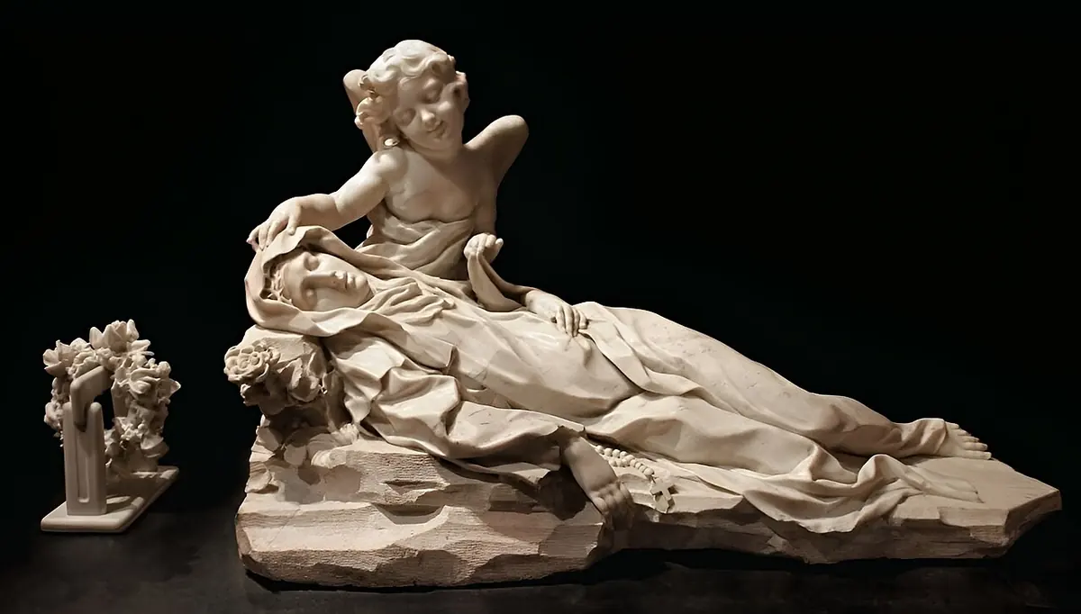 White marble sculpture of St. Rose lying back on a bed of rocks as if fainting, her head supported by a kneeling angel, against a black background