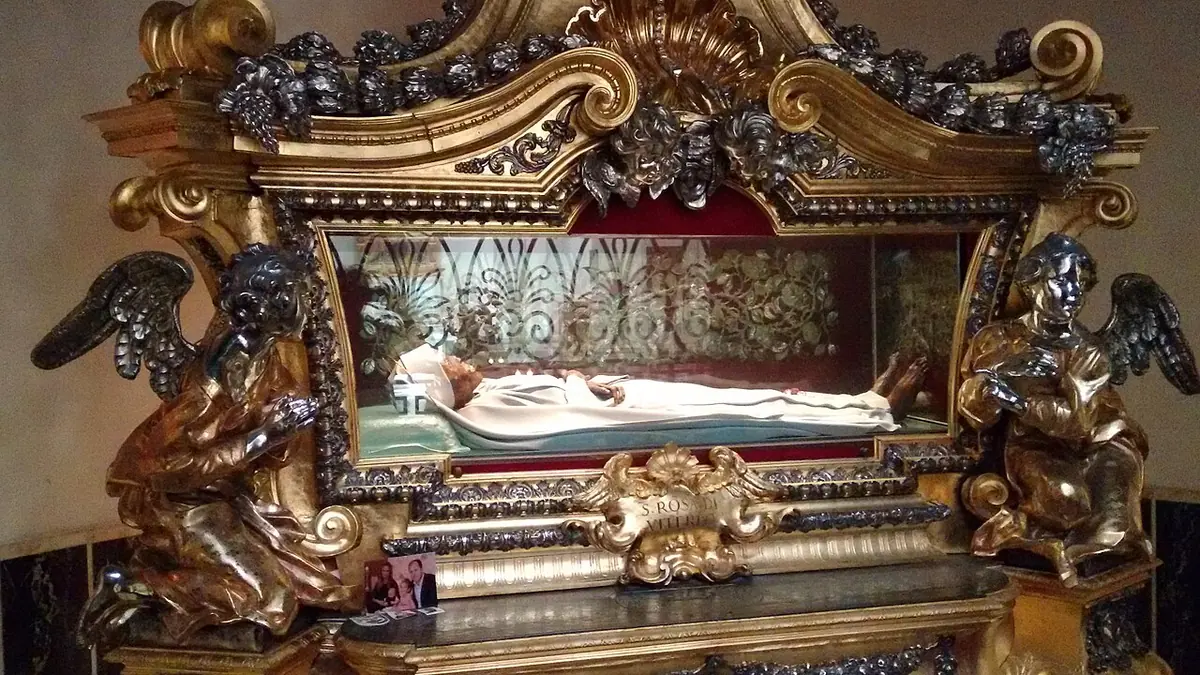 Gilded baroque reliquary with silver angels and putti holding a glass case in which the small figure of St. Rose lies dressed in white