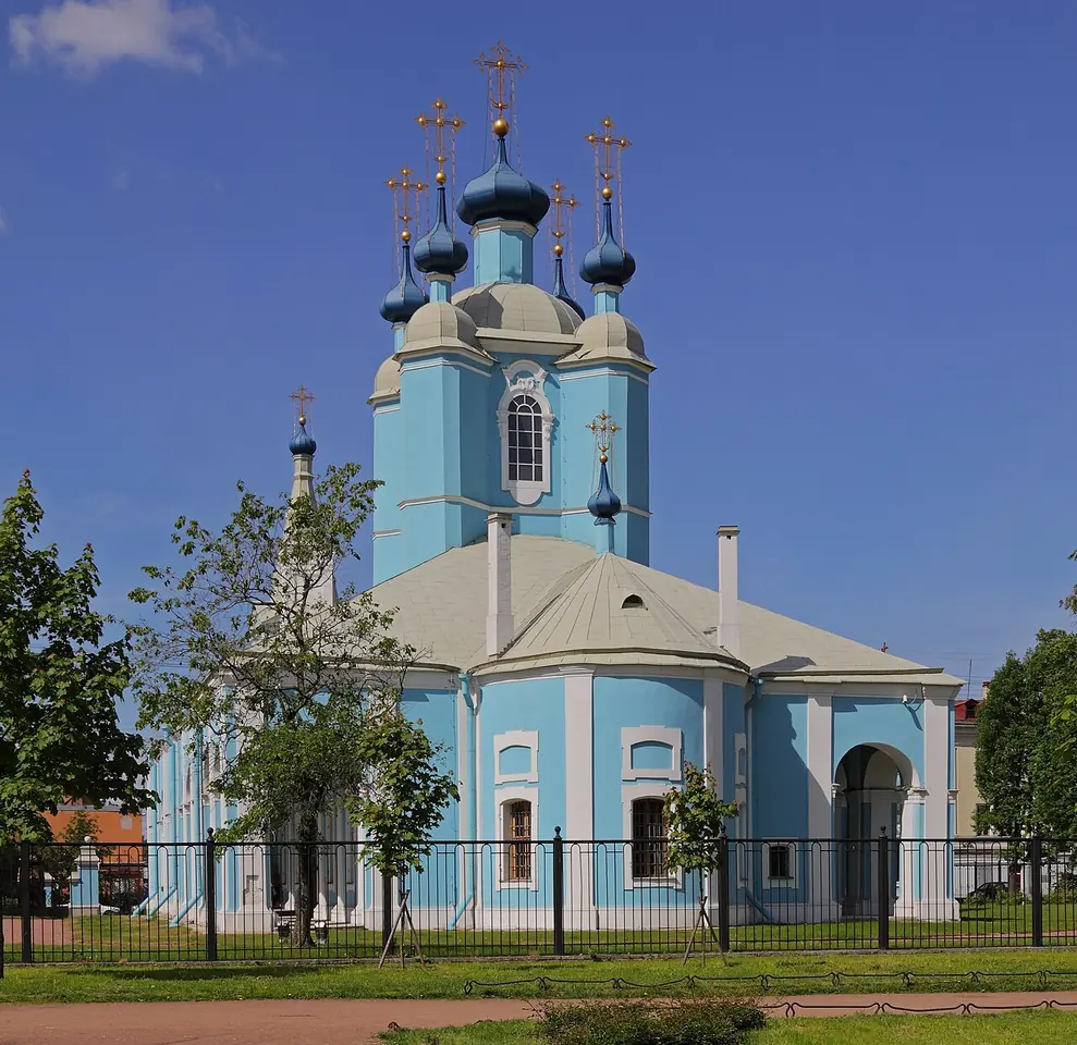 A pale blue and white baroque church with a tall bell tower and five small blue onion domes topped with gold crosses, behind an iron fence