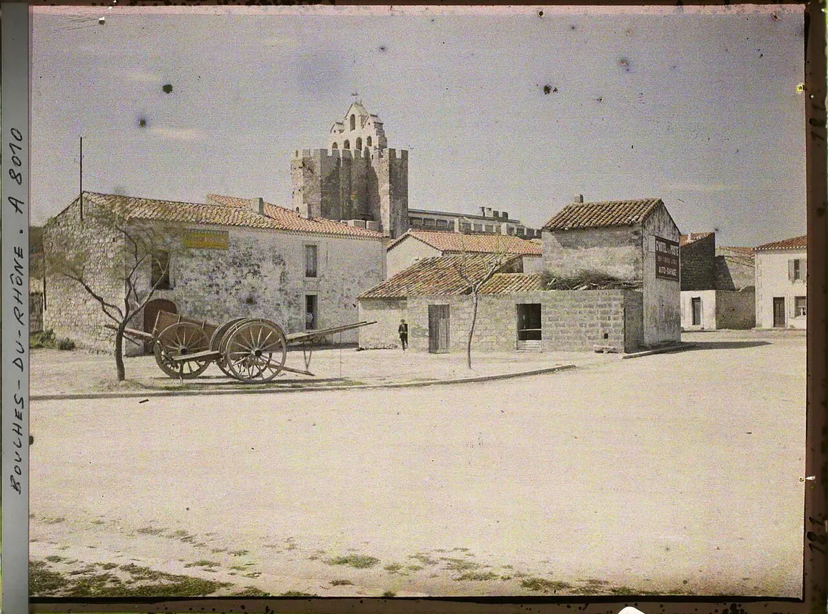 Old photograph of a fortress-like Romanesque church with battlements and a pierced bell wall rising above the low houses of a seaside village