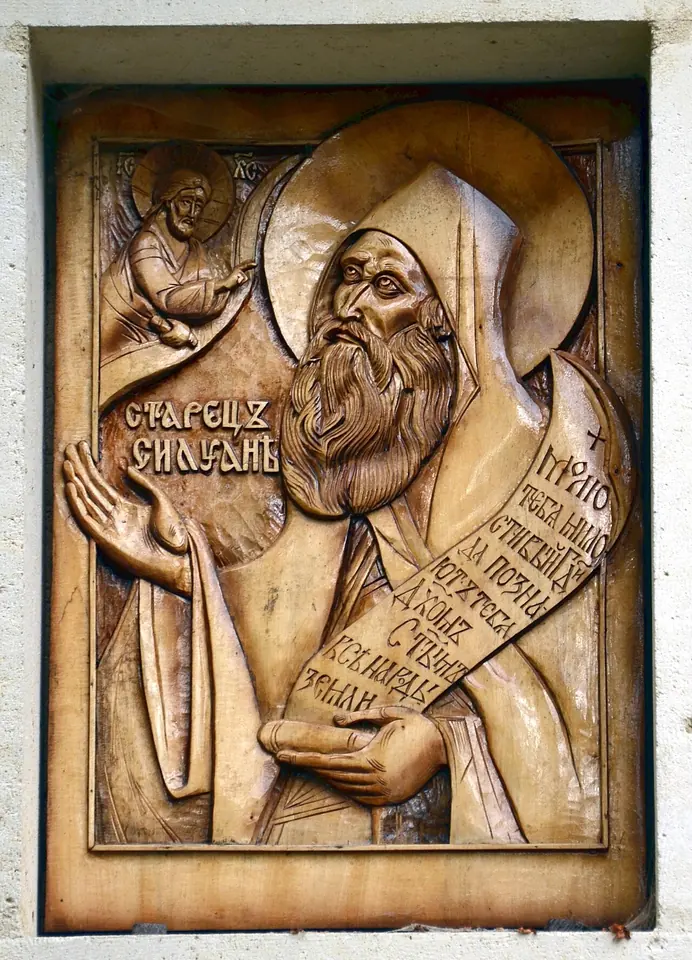 Wooden relief icon of St. Silouan bowing toward Christ in the upper corner, holding a scroll covered in Slavonic lettering