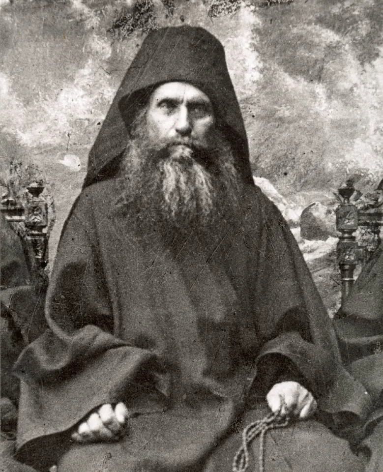 Black-and-white photograph of St. Silouan as an old monk in a black hood and habit with a long gray beard, sitting with a prayer rope in his hands