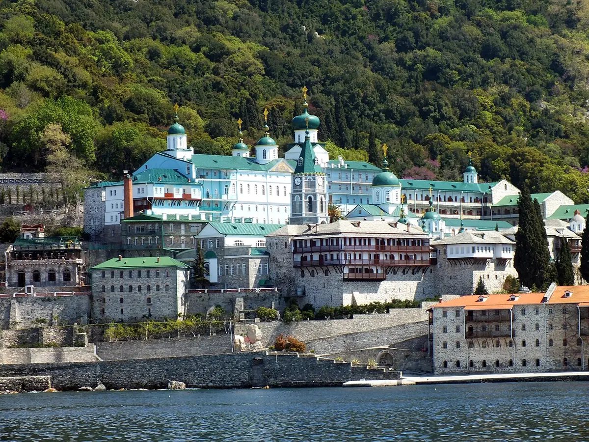 The white and pale-green buildings and green onion domes of the Russian monastery of St. Panteleimon on the shore of Mount Athos, with forested hills behind