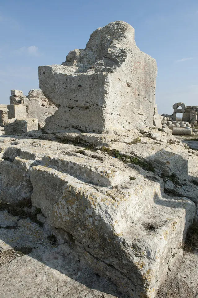 Weathered limestone base of a broken column rising from the bedrock in the middle of ruined monastery walls under a blue sky