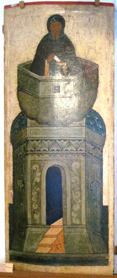 Tall Russian icon of a monk in a dark hood standing in the round top of a pale green pillar with an arched doorway at its base
