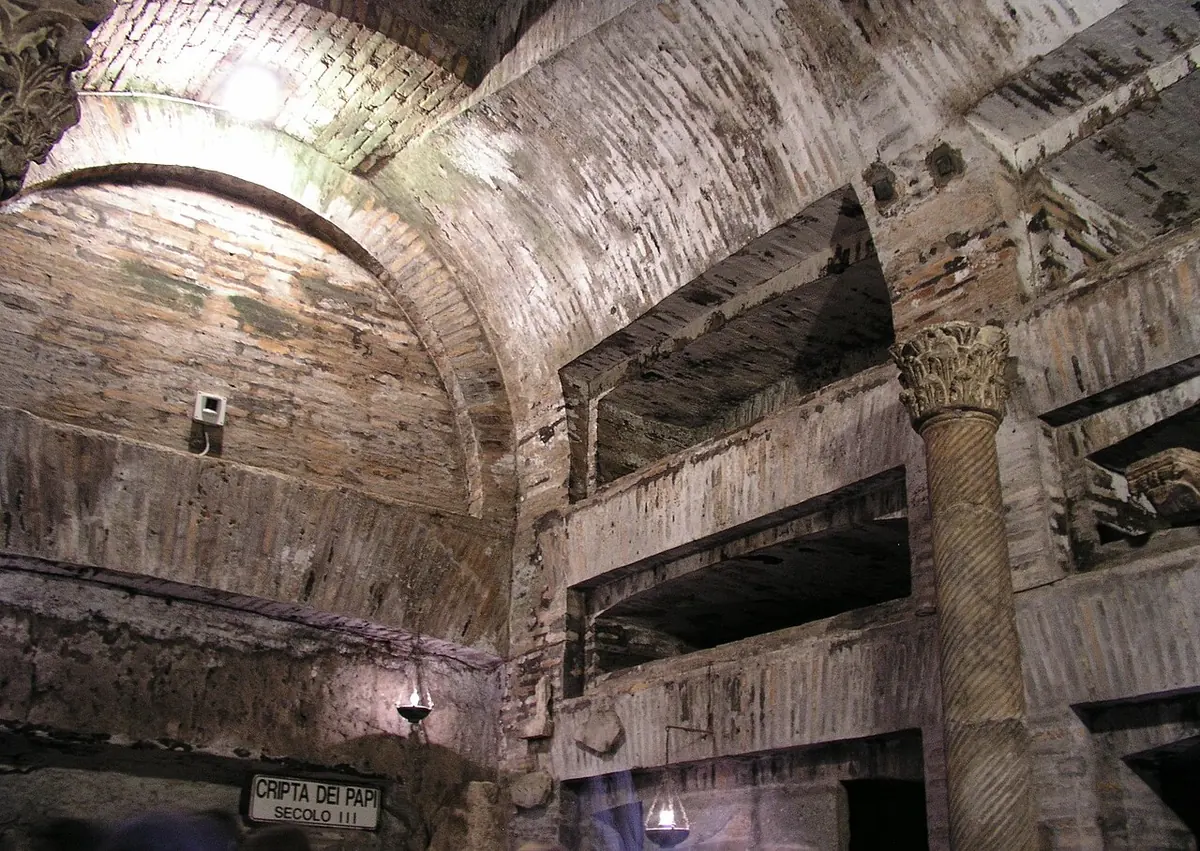 An underground chamber of pale tufa with marble slabs and inscriptions in the walls, small columns at the back and a low altar