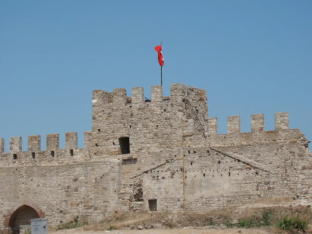 Grassy enclosure inside a ruined stone fortress, with the broken arches and walls of an old church at one side under a blue sky