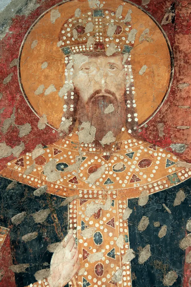 Damaged medieval fresco of a bearded king with a halo and a jeweled crown with pendants, in red and gold robes covered with pearls and jewels