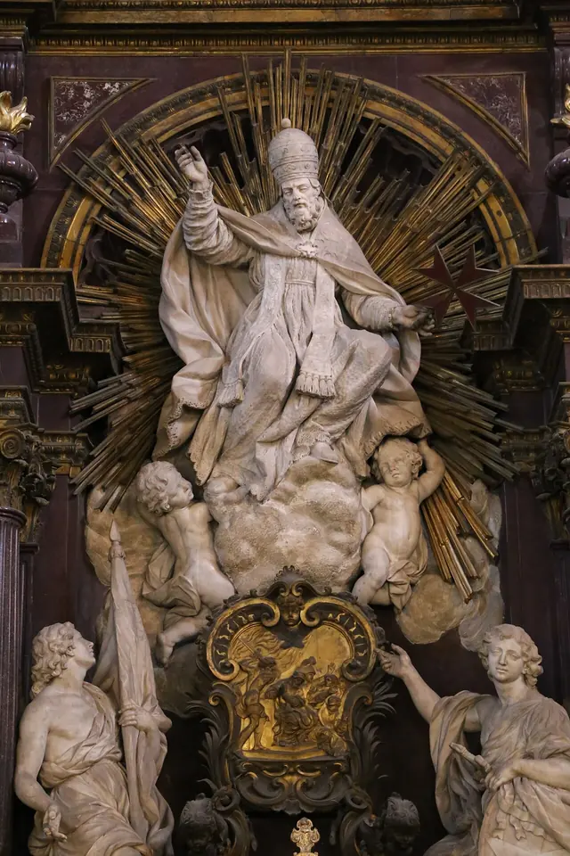 White marble statue of a pope in a miter and flowing cope raising his right hand, set against gilded rays, with angels and a gilt bronze relief below
