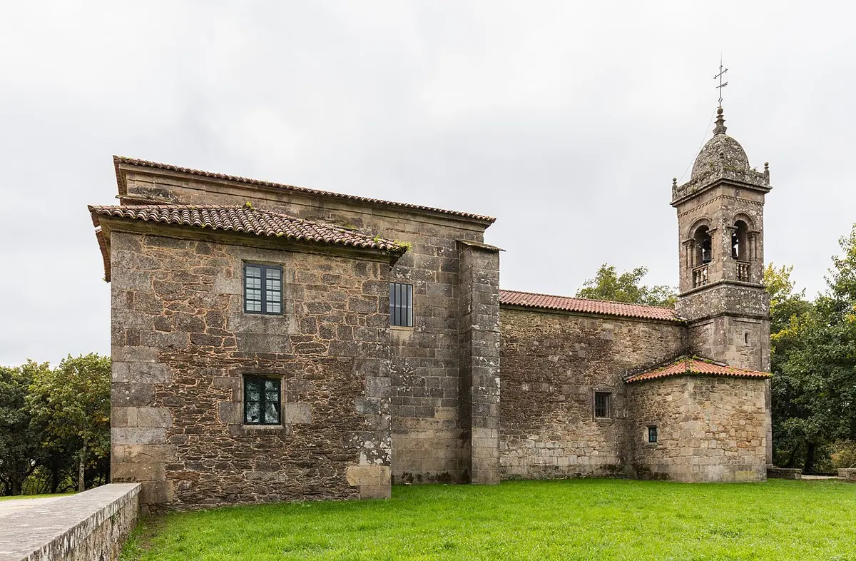 Small granite church with a tiled roof and a bell tower on a green lawn among oak trees