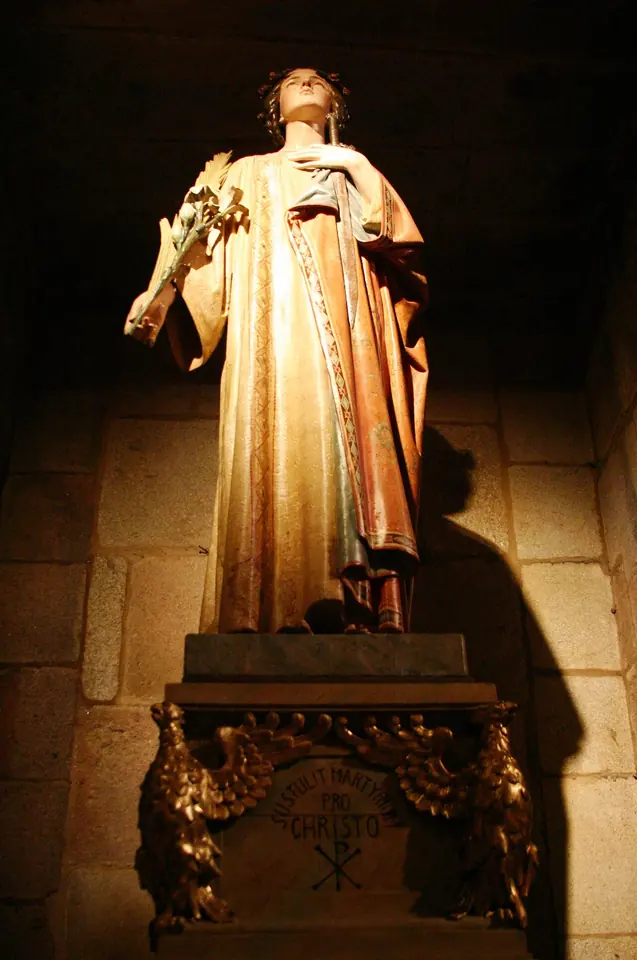 Gilded and painted wooden statue of St. Susanna lit from below, holding a palm, on a carved pedestal