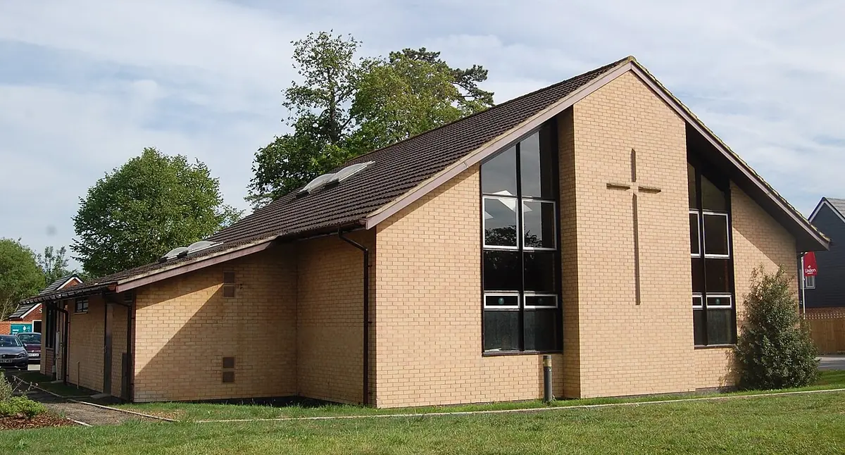 A modern brick church with a steep roof, tall windows and a large cross on its gable end