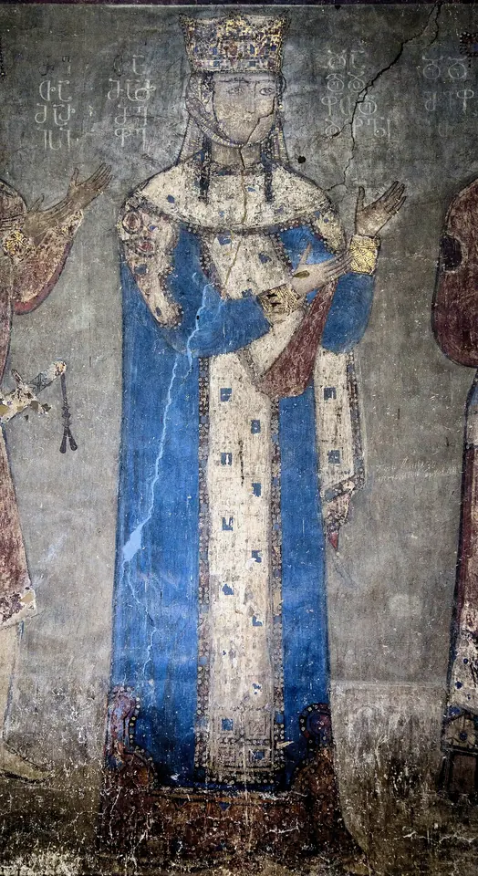 Medieval wall painting of a standing queen in a tall crown and a long blue robe with a jeweled front panel, on a gray-blue wall