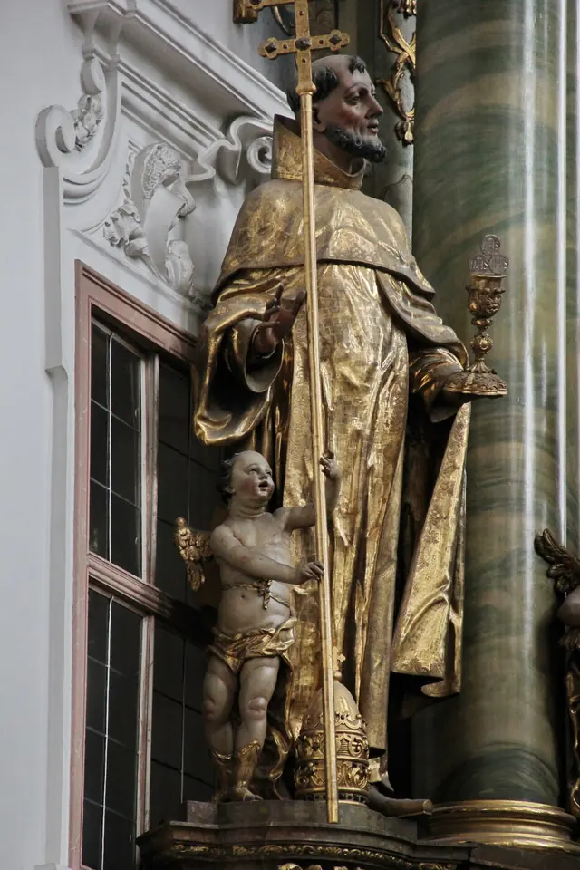 Gilded Baroque statue of a bearded saint in a dark habit and gold mantle, holding a tall cross and a chalice, with a small cherub at his feet holding a papal tiara