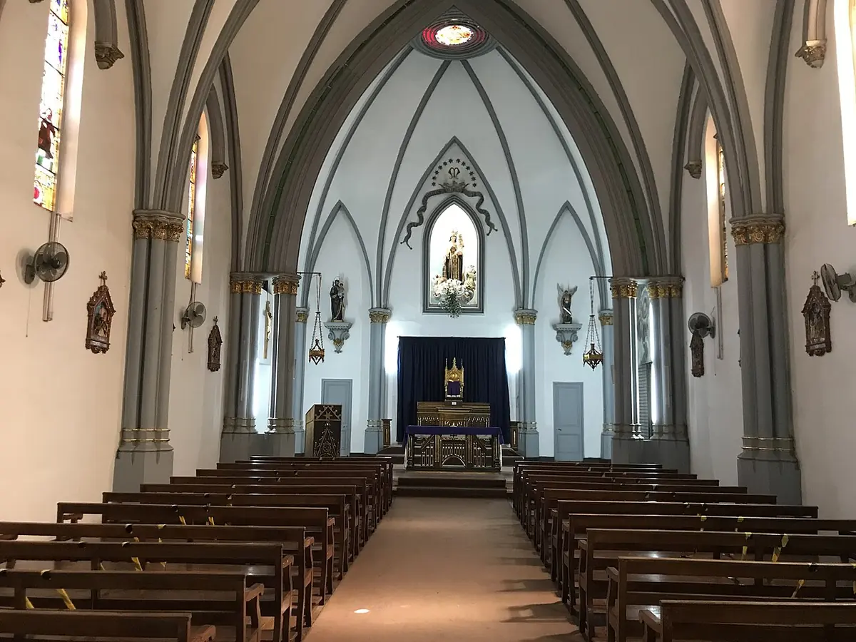 Interior of a small Gothic-revival church with gray pointed arches, wooden pews and a statue of Our Lady above the altar