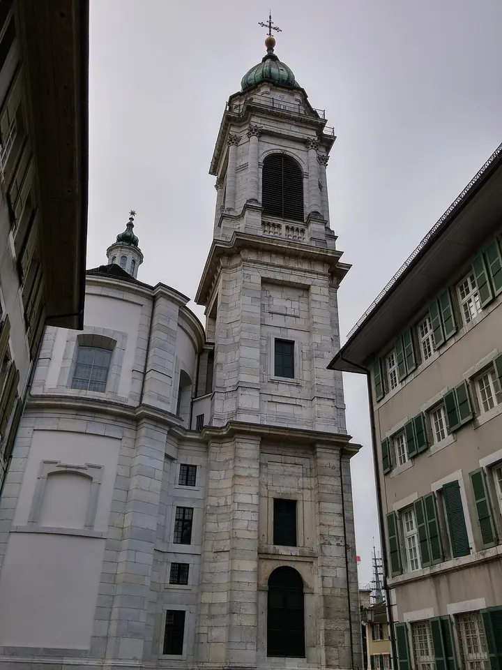 The pale stone bell tower and dome of the Baroque cathedral of St. Ursus in Solothurn, seen from a narrow street