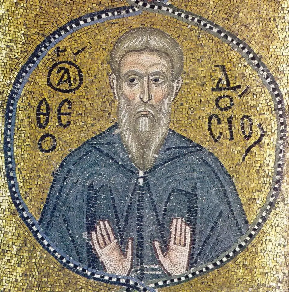 Byzantine gold-ground mosaic of a monk with a long gray beard in a blue-gray habit, both hands raised in prayer, inside a round border with his name in Greek