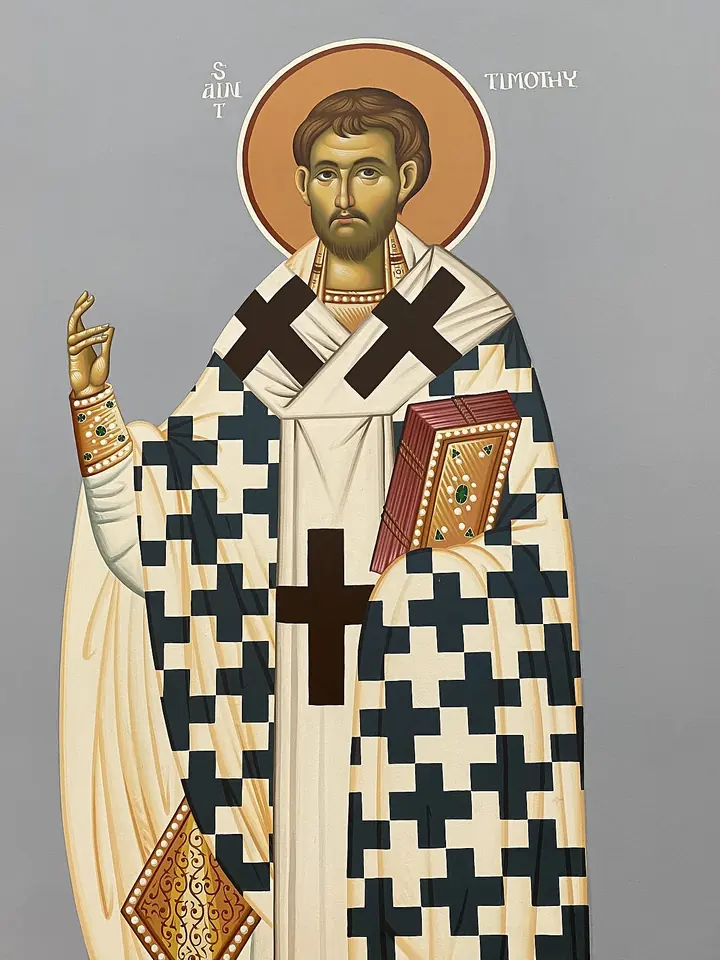 Modern Byzantine-style icon of St. Timothy as a young dark-bearded bishop in a white stole with black crosses, blessing with one hand and holding a red Gospel book in the other