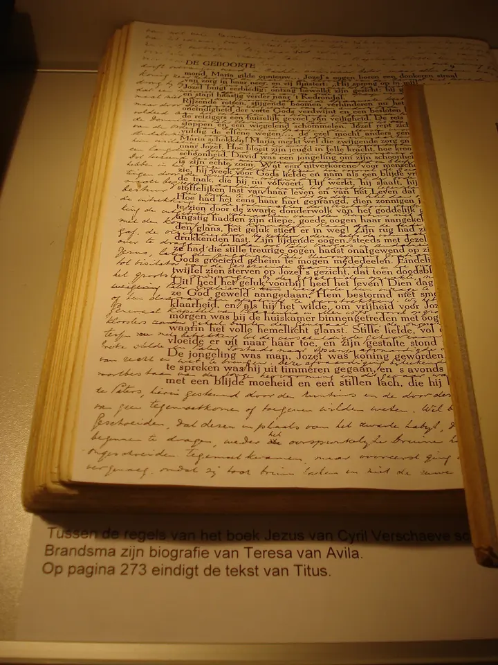 An open printed book displayed in a case, its pages filled with small handwriting squeezed between the printed lines