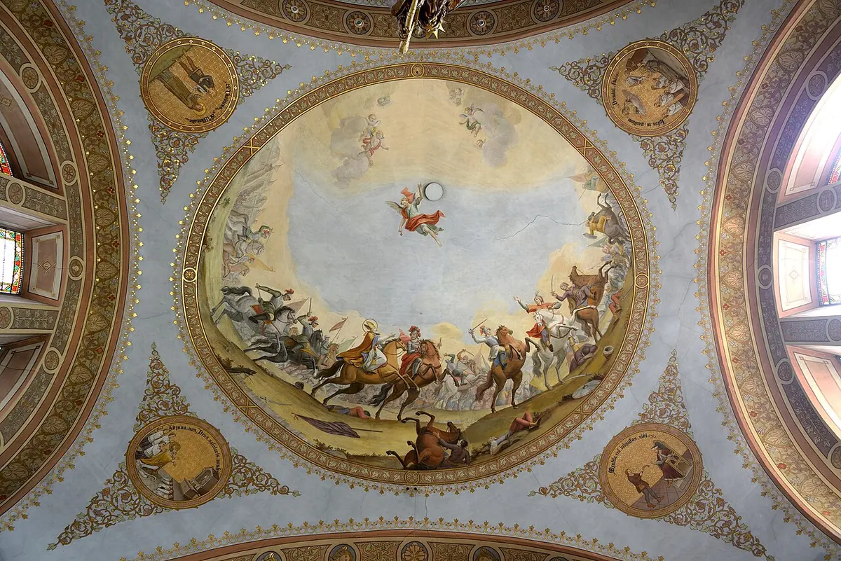 Oval ceiling fresco of a battle on a plain with horsemen fighting, and a small figure in the sky above, inside a decorated domed vault