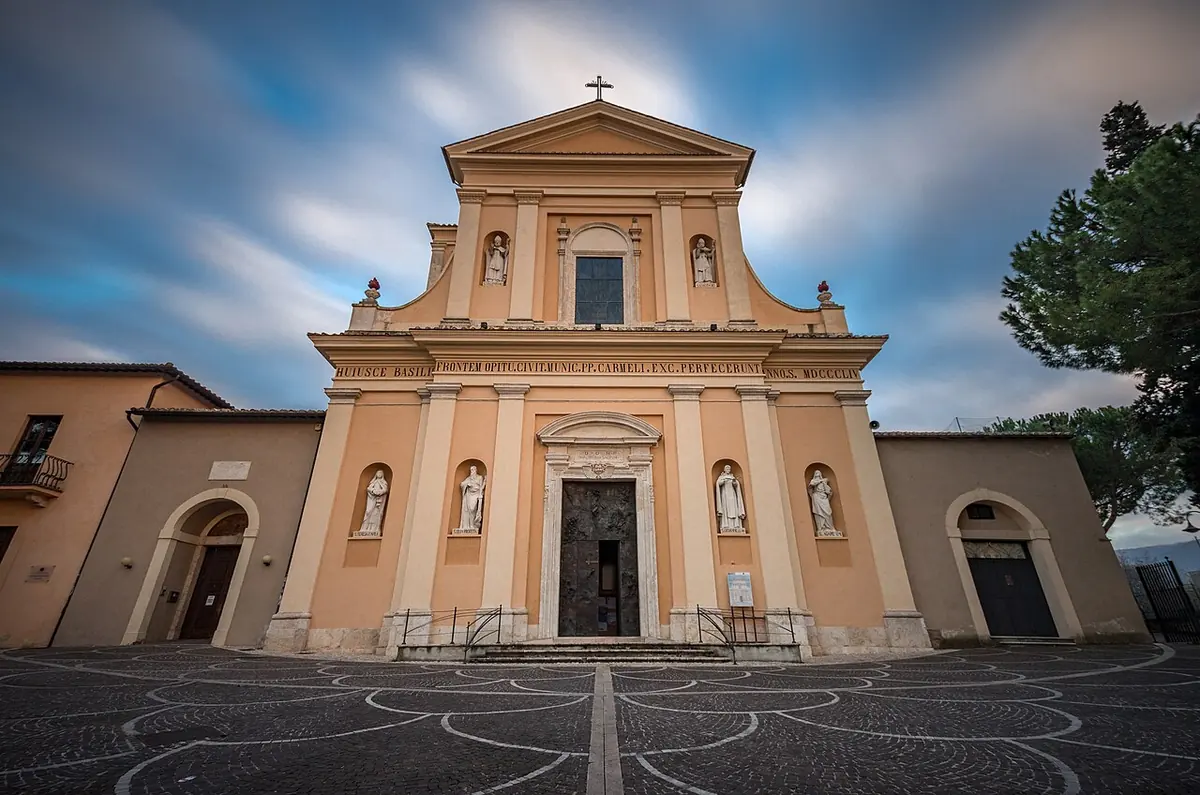 The cream-colored classical facade of the Basilica of San Valentino in Terni, with statues in niches, under a blue sky with clouds